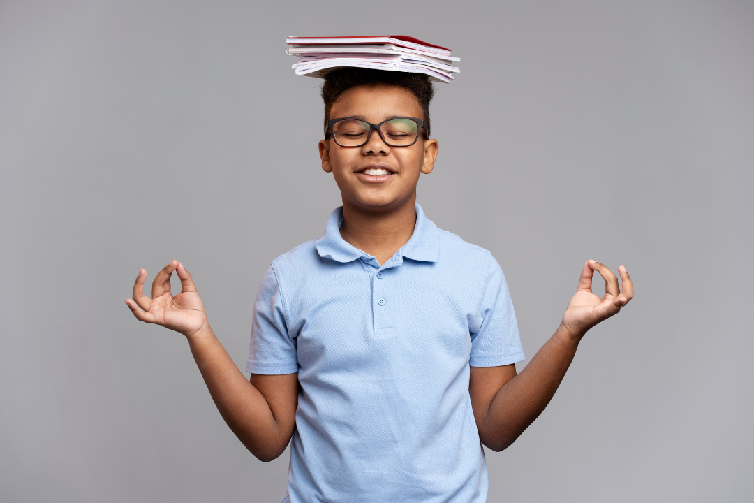 Menino meditando com livros na cabeça. Aulas de yoga no Kidsa: Como funciona? Foto Reprodução: Freepik