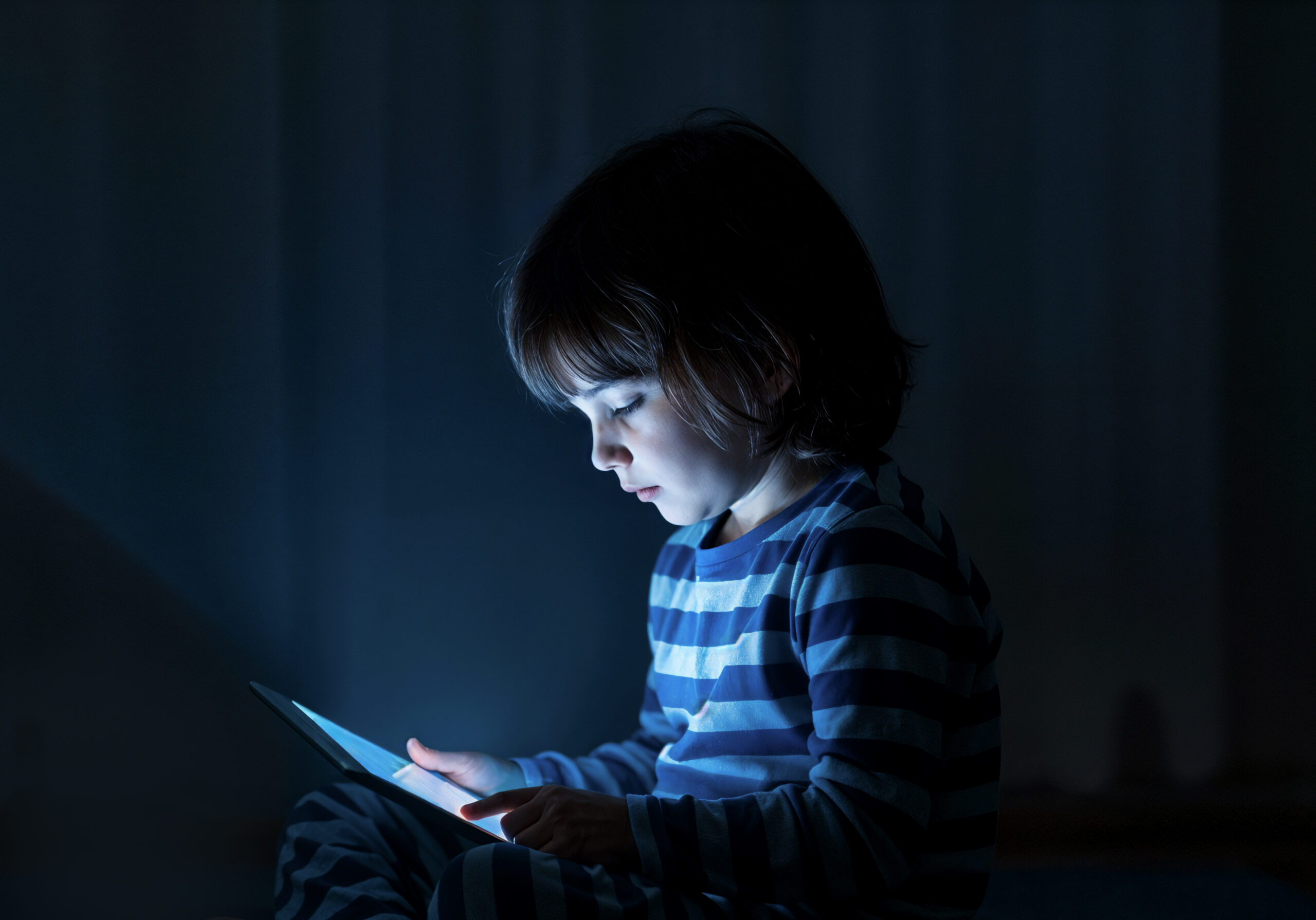 Menino utilizando tablet durante a noite. Como equilibrar telas, brincadeiras e aprendizado na infância? Foto/Reprodução: Freepik.