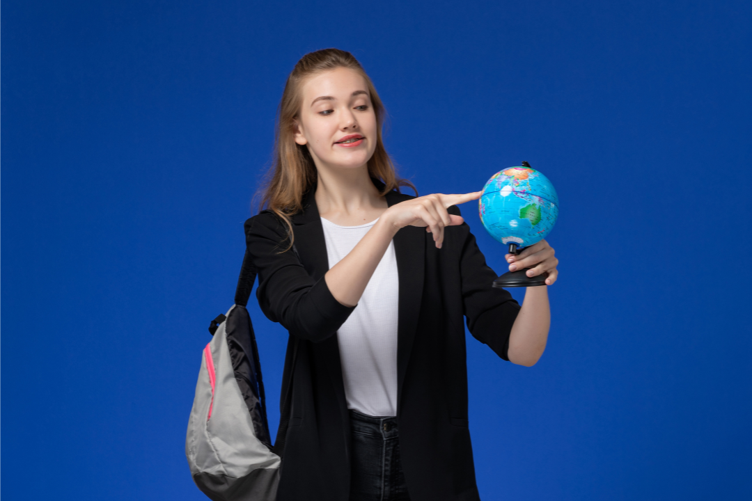Menina adolescente apontando para um globo. Como o inglês pode ajudar adolescentes no intercâmbio? Conheça os principais benefícios. Foto/Reprodução; Freepik.