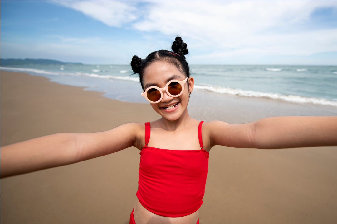 Menina de óculos sorrindo em uma praia. Como manter o inglês nas férias escolares? 10 dicas para continuar aprendendo! Foto/Reprodução: Freepik.