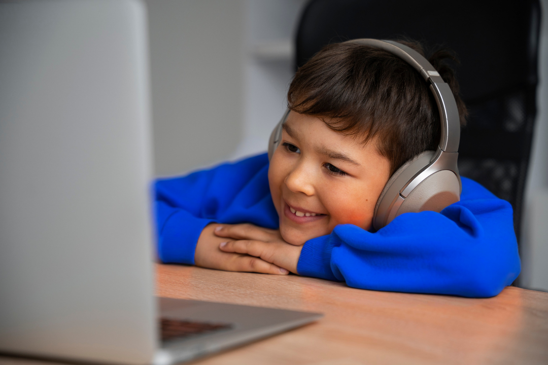Menino assistindo aula pelo computador com fone de ouvido. Tecnologia no ensino de inglês infantil: benefícios e impacto. Foto/Reprodução: Freepik.