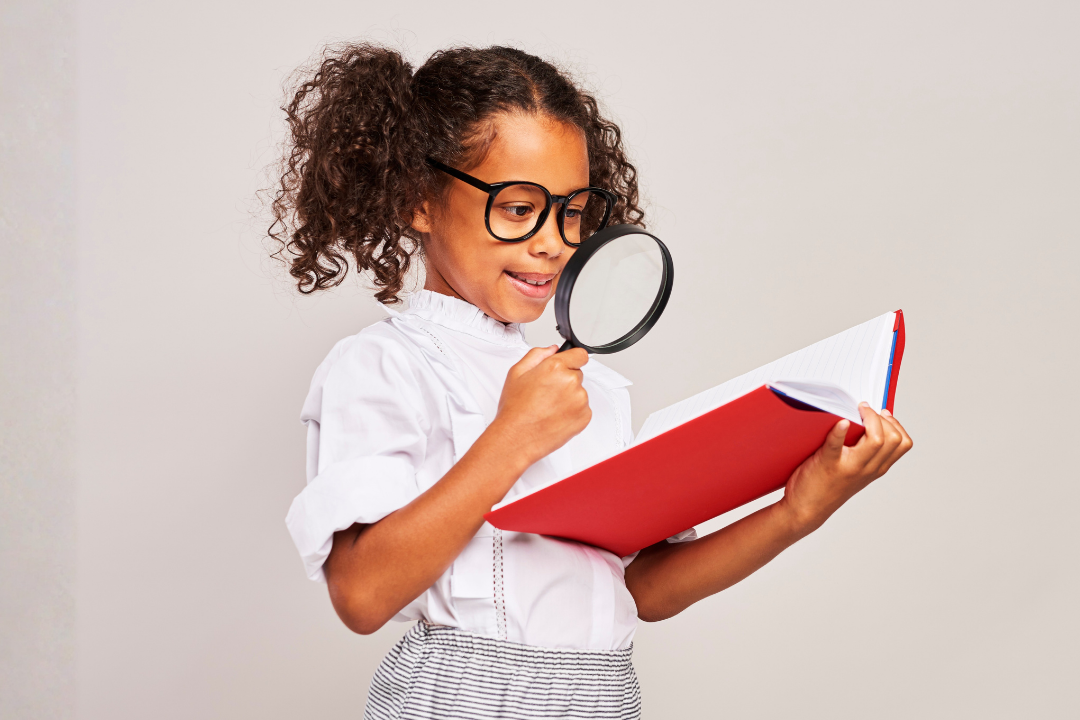 Menina analisando um livro com uma lupa. Crianças precisam estudar gramática para aprender inglês? Foto/Reprodução: Freepik.
