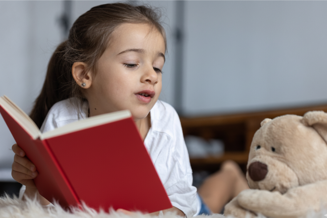 Menina lendo um livro com um ursinho de pelúcia. Contação de história em inglês: por que ela ajuda no aprendizado? Foto/Reprodução: Freepik.