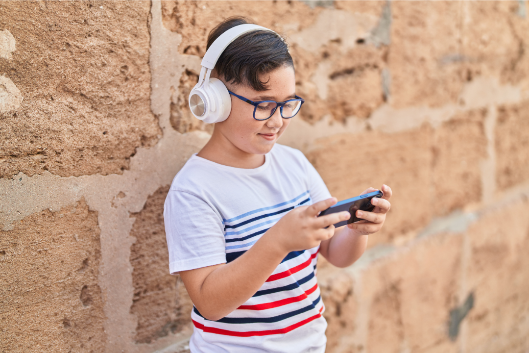 Menino sorrindo com confiança enquanto usa o celular. 7 formas de aprender inglês usando celular (para crianças e adolescentes). Foto/Reprodução: Freepik.