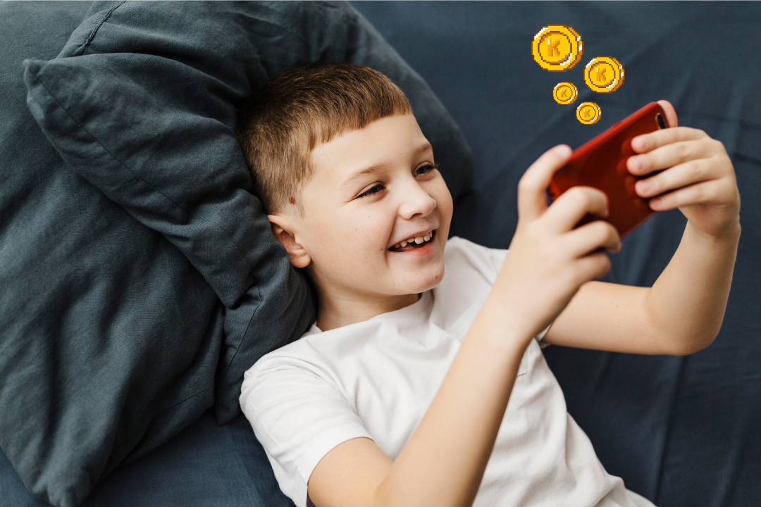 Menino utilizando o celular e brincando. O que são e como funcionam as Kidsa Koins? Foto/Reprodução: Freepik e Canva.