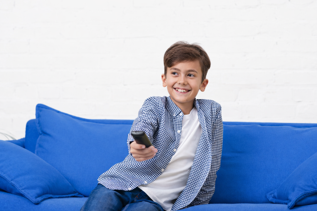 Menino feliz com o controle remota na mão. Crianças aprendem inglês assistindo desenhos? Entenda o que realmente funciona! Foto/Reprodução: Freepik.