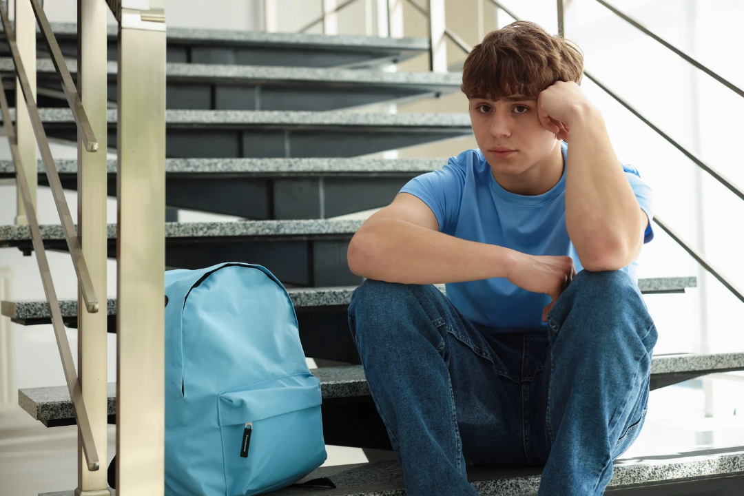 Adolescente em ambientee escolar sentado em uma escada e pensativo. Por que adolescentes têm vergonha de falar inglês? Foto/Reprodução: Freepik.