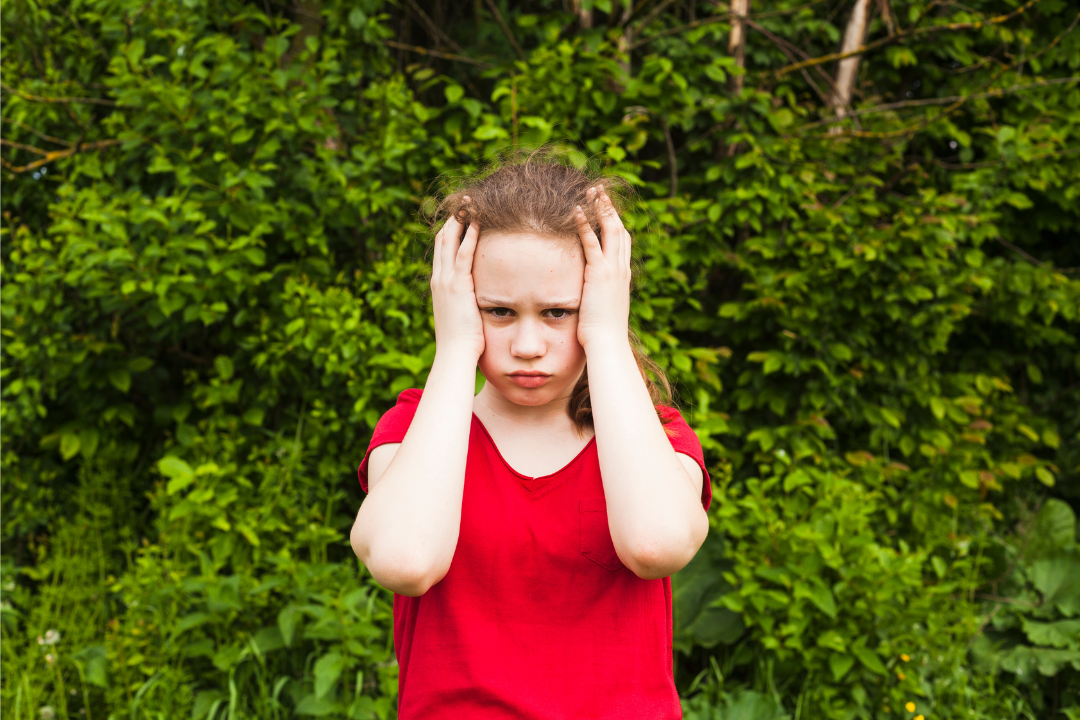 Menina triste com as mãos na cabeça. Meu filho não quer falar inglês em casa. Devo insistir? Foto/Reprodução: Freepik.