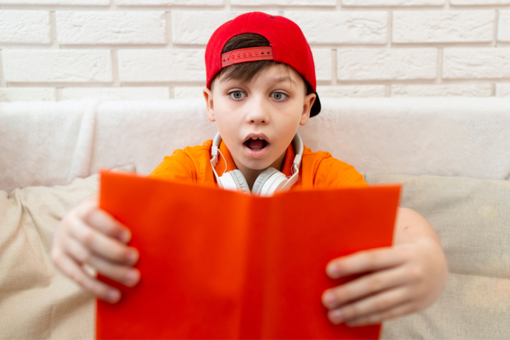 Menino com livro aberto e expressão de surpresa. Aprendizagem não linear: por que aprender inglês de diferentes formas faz bem para o desenvolvimento? Foto/Reprodução: Freepik.