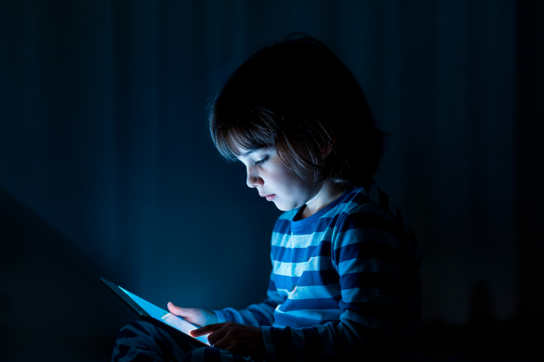 Menino utilizando tablet a noite. Como equilibrar telas, brincadeiras e aprendizado na infância? Foto/Reprodução: Freepik.